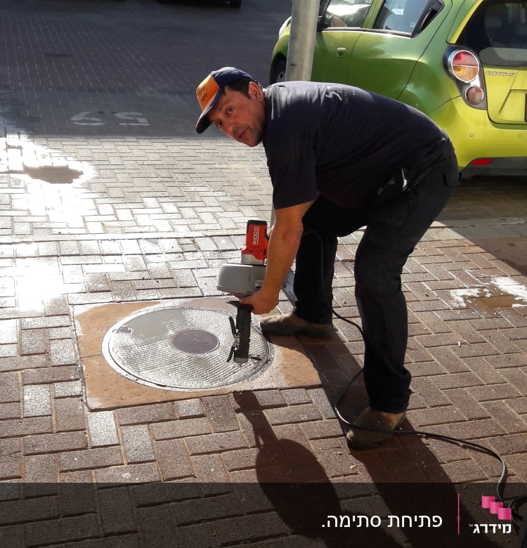 אדם משתמש בכלי עבודה לפתיחת ביוב ברחוב